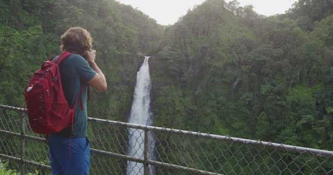 Hawaii tourist taking pictures of rainforest while hiking the famous Akaka Falls State Park on Hawaii, Big Island, USA. Man traveler using DSLR camera on travel. Slow motion.