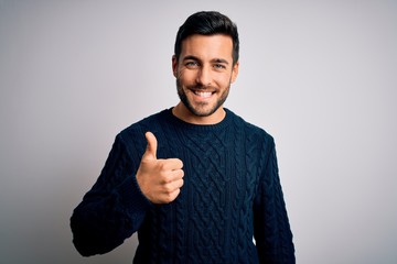 Young handsome man with beard wearing casual sweater standing over white background doing happy...