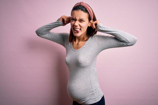 Young Beautiful Teenager Girl Pregnant Expecting Baby Over Isolated Pink Background Smiling Pulling Ears With Fingers, Funny Gesture. Audition Problem