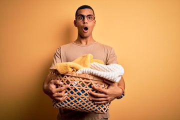 Young handsome african american man doing housework holding wicker basket with clothes scared in shock with a surprise face, afraid and excited with fear expression