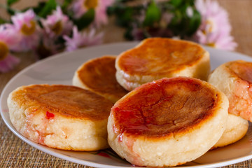 Cottage cheese pancakes with sour cream and jam on a brown background. Breakfast dish next to flowers.