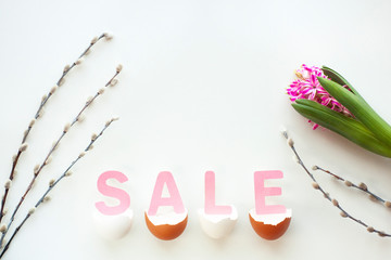 Pink letters SALE lie in broken egg shell, hyacinth flower and pussy-willow twigs on white desk. Spring, Easter sale concept. Flat lay, top view, copy space.