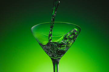 Martini pouring in a cocktail glass. Extra dry martini. Vermouth wine. Alcohol cocktail Beautiful green emerald background. 