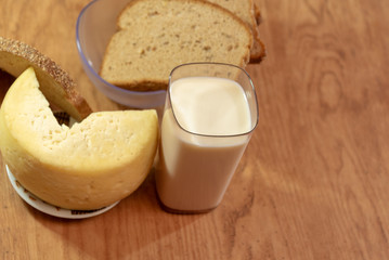A glass of milk and a piece of cheese and slices of rye bread under a yellowed wooden table
