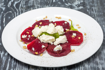Snack of slices of boiled beetroot with goat cheese, lettuce and pine nuts in restaurant serving