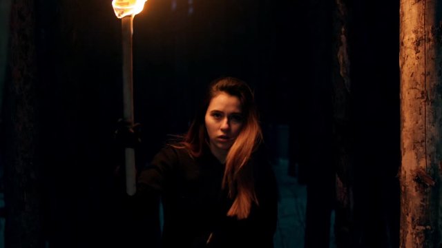 Young pretty woman traveler walking in the woods at night time holding a torch