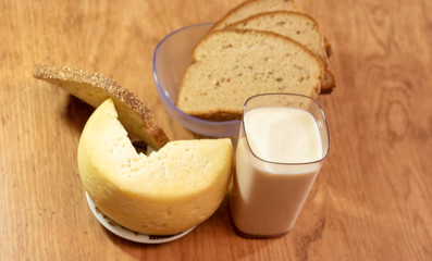 A glass of milk and a piece of cheese and slices of rye bread under a yellowed wooden table
