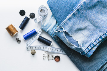 Handicraft, clothing repair. Ripped blue jeans sewing accessories white background. The concept of...
