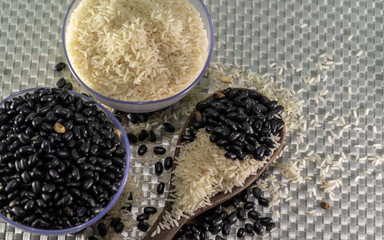 Bowls with grains of rice and beans mixed with a wooden spoon on silver background