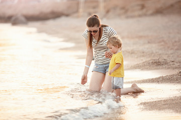 Happy mother and son play on the beach. Mom and baby play in the sea. Mom play with a toddler on the seaside. Mother's love. Lifestyle. Sunny day. Summer rest. Family vacation. Mothers day.