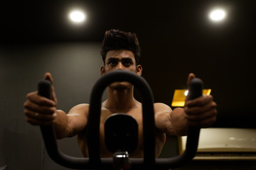 An young and handsome Indian Bengali brunette man with muscular body doing exercise in a multi gym....