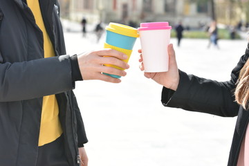 TWO Woman's Hands holding stylish reusable eco coffee cups outdoors. .