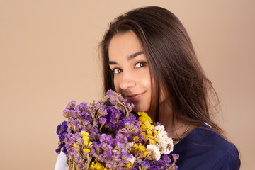 Portrait of a young beautiful girl in the studio. Dressed in a blue dress. Holding a bouquet of...