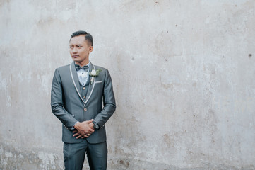 Selective focus of groom is standing with concrete wall background. Wedding concept.