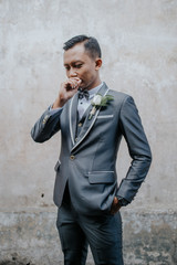 Selective focus of groom is standing with concrete wall background. Wedding concept.