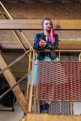 Portrait of a young girl with pink hair standing on the rusty stairs inside of collapsed building surrounded by ruins