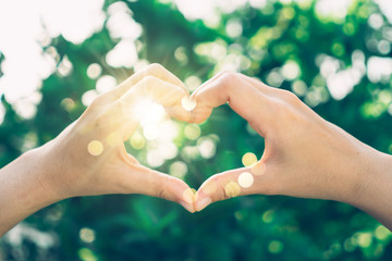 Woman hand do heart shape on green nature tropical background.