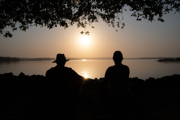Fototapeta na wymiar Young couple sitting on a rock near the sea and watching the sun, dawn