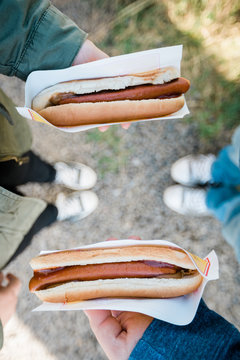 Two People Holding Hotdogs From Above