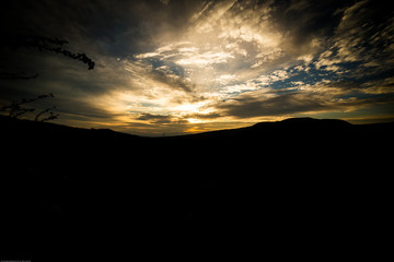 Amanecer entre las lomas. Cielo calido y con nubes en siluetas