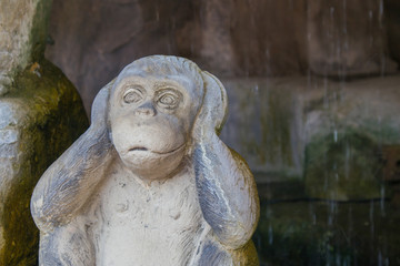 Fototapeta na wymiar Monkey statue sit and close her ears in a cave with waterfall on background