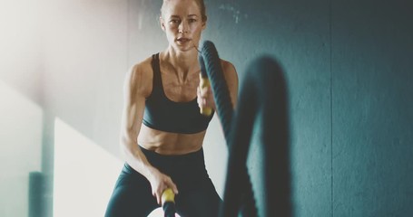 Fit attractive woman working out with battle ropes in the gym, intense focused woman training hard to achieve her fitness dreams - Powered by Adobe