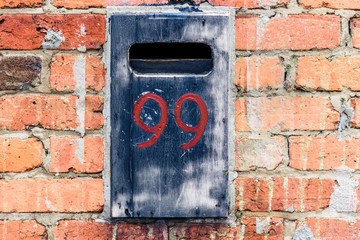 The number 99 is attached to a weathered letter box on a brick wall