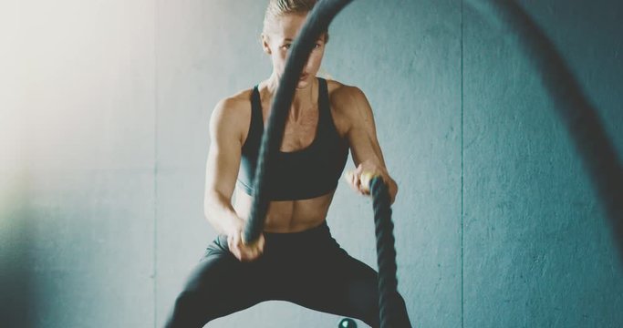 Fit attractive woman working out with battle ropes in the gym, intense focused woman training hard to achieve her fitness dreams