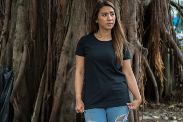 Young woman wearing black t shirt posing at park in front view, suitable for mock up template, background, etc.