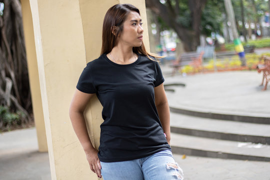 Young woman wearing black t shirt posing at park in front view, suitable for mock up template, background, etc.