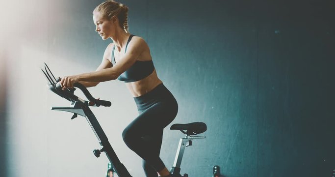 Fit attractive woman working out on a stationary bike in the gym, focused woman getting a cardio workout to achieve her fitness goals