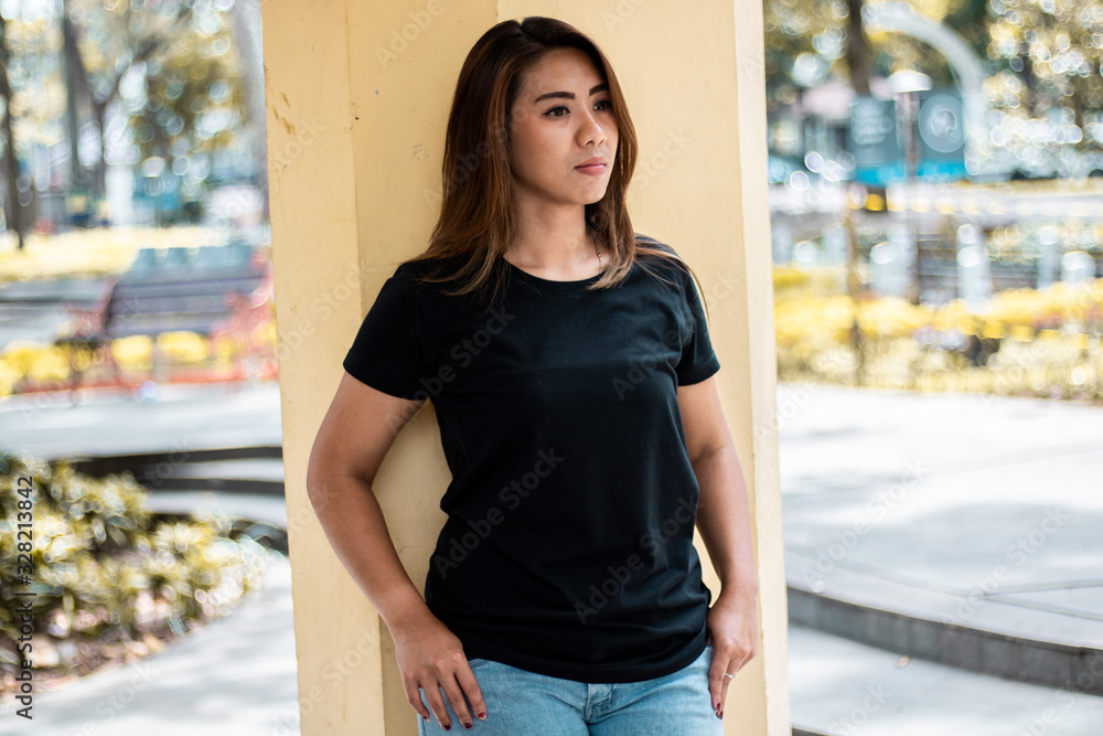 Wall mural Young woman wearing black t shirt posing at park in front view, suitable for mock up template, background, etc.