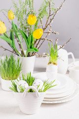 Fototapeta na wymiar Festive composition Easter eggs in glasses white dishes and willow tulips on a white table. Happy Easter concept.