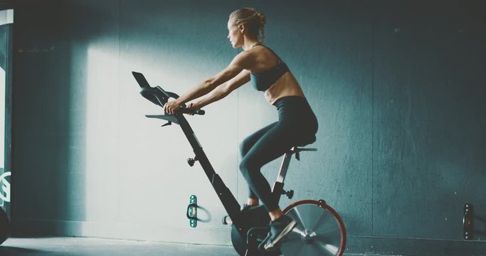Fit attractive woman working out on a stationary bike in the gym, focused woman getting a cardio workout to achieve her fitness goals