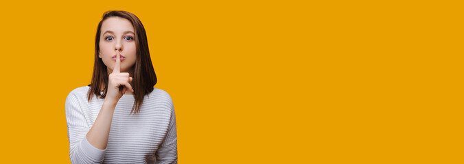 Charming caucasian girl gesturing the silence sign on yellow wall with freespace
