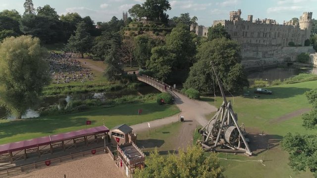 Aerial static shot of trebuchet firing whilst crowd watches at Warwick Castle