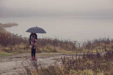 young girl with black umbrella on background dark foogy lake