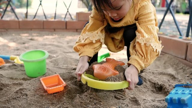 Happy little child girl having fun playing with plastic toys sitting in the sandbox on a sunny summer day.