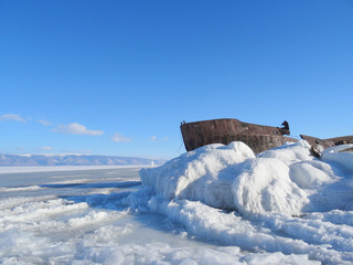 an old rusty ship frozen in ice against a mountain range and blue sky