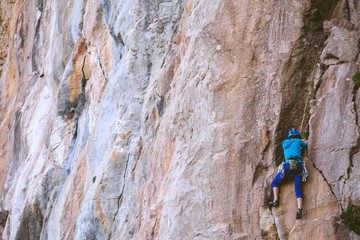 A woman in a helmet climbs a beautiful orange rock.