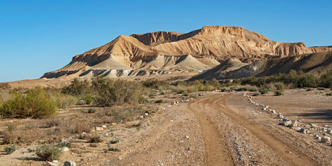 the jeep road running through the nahal zin stream bed in the negev in israel with stunning barren desert mountains and blue sky in the background