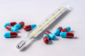 Closeup of an analog thermometer with pills spilled around it