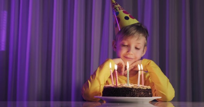 Happy child looks at a cake with candles. Child looks at the cake and makes a birthday wish. Boy celebrates his birthday. Happiness concept