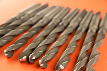 close-up of metal drills on a bright orange surface, some objects are out of focus. Metal cutting...