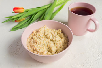 Nutritious oatmeal for breakfast served on in pink bowl and cup of black tea on white background