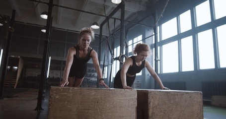 Slow motion two young beautiful female athletes working out, doing push-ups and clapping together...