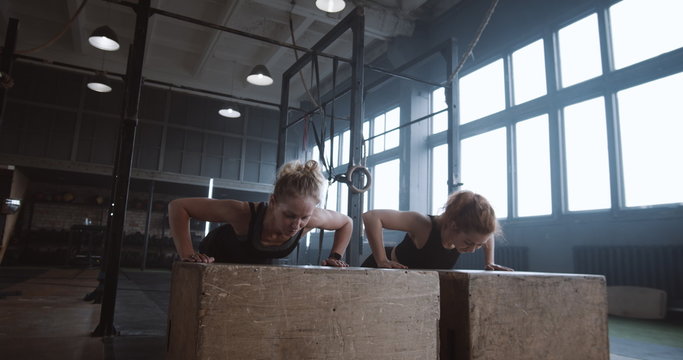 Slow motion two young beautiful female athletes working out, doing push-ups and clapping together in atmospheric gym.