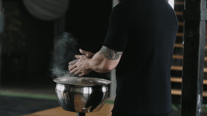 Close-up back view male weight lifter athlete applying talc powder before exercising in large...
