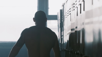 Silhouette of young male athlete alone in dark gym changing room hitting locker, overcoming failure stress and pressure.