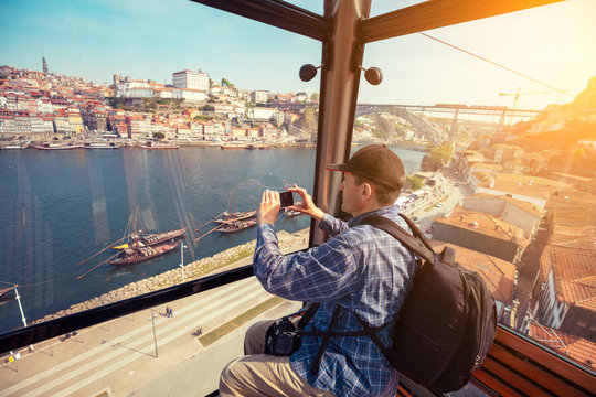Male tourist sitting in the cabin of the cable car and taking pictures of the historic center of Porto